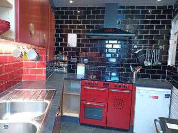 Die Küche hat coole schwarze und rote Fliesen, dazu passende rote Schränke und einen roten Ofen, eine Spüle aus Edelstahl, Utensilien an der Wand, einen Minikühlschrank und moderne Beleuchtung.
