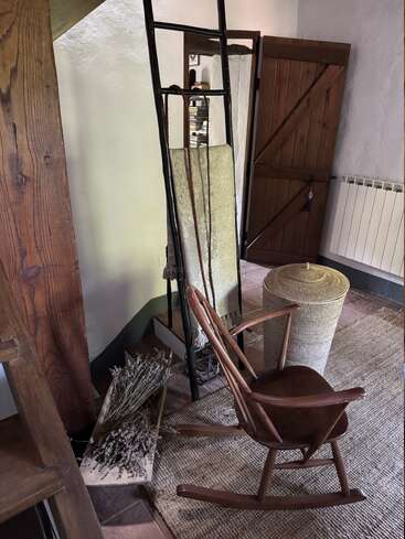 A cozy corner with a wooden rocking chair, rustic basket, ladder, dried lavender, rug, mirror, and wooden door, creating a warm, inviting, vintage atmosphere.