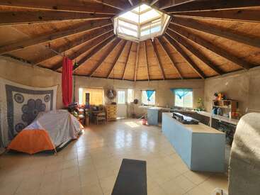 La salle ronde spacieuse dispose d'un haut plafond en bois avec une lucarne, d'un sol carrelé, d'un coin cuisine, d'une tente, d'étoffes aériennes, de rideaux bleus, d'un bureau et de décorations murales.