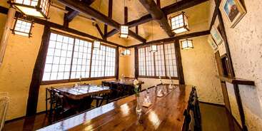 Esta imagen muestra un acogedor comedor de estilo japonés con vigas de madera, ventanas de papel shoji, iluminación con farolillos, mesas y sillas de madera, que crean un ambiente cálido y acogedor.