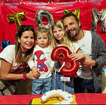 Une joyeuse famille de quatre personnes pose ensemble lors de la fête d'anniversaire d'un enfant. Le petit garçon fête ses trois ans. Des décorations colorées, des ballons et un gâteau viennent compléter la fête.