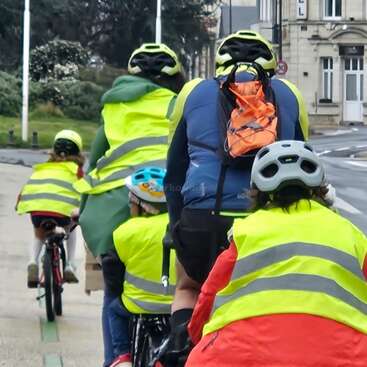 Eine Gruppe von Radfahrern, sowohl Erwachsene als auch Kinder, tragen leuchtend gelbe reflektierende Westen und Helme, während sie gemeinsam auf einer Straße in der Stadt fahren und für Sicherheit werben.