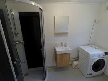 Cette photo montre une salle de bains simple équipée d'une douche vitrée, d'un petit lavabo avec meuble, d'un miroir, d'un lave-linge et de lessive, le tout sur un sol propre et clair.