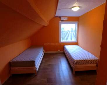 Cette photo montre une petite chambre aux murs orange, avec deux lits simples de chaque côté, un sol en bois et une fenêtre donnant sur un champ.