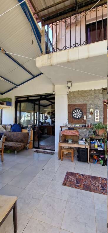 Esta imagen muestra un patio interior acogedor y ecléctico con suelo de baldosas, diana en una pared de piedra, sofás, alfombras, plantas, estanterías y puertas correderas de cristal.