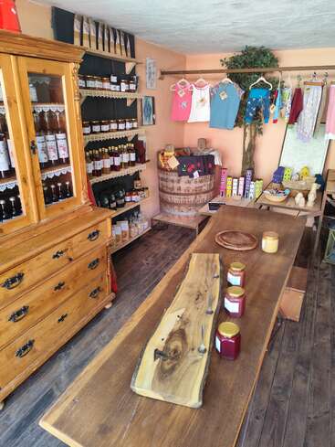 This cozy shop features homemade preserves, syrups, handcrafted wooden decor, children’s clothes, candles, and birdhouses, all displayed on rustic wooden furniture and shelves.
