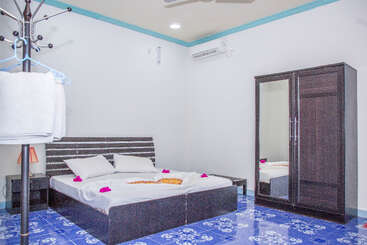 Das saubere, moderne Schlafzimmer verfügt über ein Doppelbett mit weißer Bettwäsche, dunkle Holzmöbel, geblümte Bodenfliesen, eine Klimaanlage und Handtücher auf einem Kleiderständer.