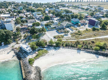 Dieses Luftbild zeigt ein friedliches Küstendorf mit Häusern, Grünflächen, einem weißen Sandstrand, klarem türkisfarbenem Wasser und einem Boot, das in der Nähe der Küste ruht.