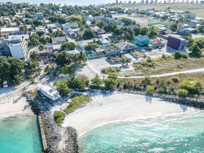 Dieses Luftbild zeigt ein friedliches Küstendorf mit Häusern, Grünflächen, einem weißen Sandstrand, klarem türkisfarbenem Wasser und einem Boot, das in der Nähe der Küste ruht.