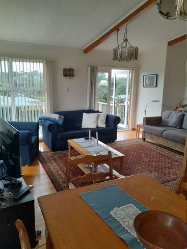 A cozy living room with blue sofas, patterned rug, wooden furniture, large windows, sliding doors, chandelier, TV, and dining table, overlooking a scenic outdoor view.