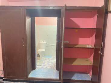 Dieses Bild zeigt einen braunen Holzschrank mit offenen Türen, die Regale und einen Durchgang offenbaren, der direkt in ein kleines Badezimmer führt, in dem eine Toilette zu sehen ist.