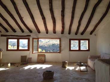 L'image représente une pièce spacieuse aux murs et au plafond blancs, avec des poutres en bois, des fenêtres et un canapé, la lumière naturelle pénétrant par la fenêtre ouverte.