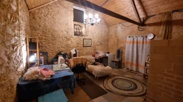 Cette pièce confortable est dotée de murs en pierre rustiques, d'un plafond en bois, d'un poster représentant Bouddha, d'une machine à coudre, d'une coiffeuse, de tapis, d'un éclairage tamisé et de sièges confortables, créant ainsi une atmosphère sereine et créative.