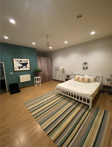 Ein geräumiges, gemütliches Schlafzimmer mit Holzböden, einem gestreiften Teppich, einem weißen Bett, einer türkisfarbenen Akzentwand, abstrakter Kunst, einer Topfpflanze und minimalistischer Einrichtung unter warmer Deckenbeleuchtung.