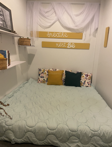 Ein gemütliches Schlafzimmer mit einem großen, ordentlich gemachten Bett, bunten Kissen, motivierenden Wandschildern, Bücherregalen, geflochtenen Körben und transparenten Vorhängen, die die weißen Wände schmücken.