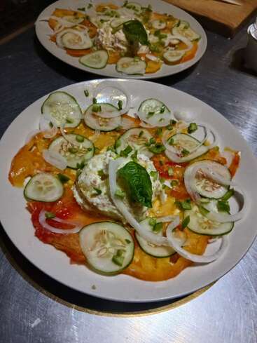 Deux assiettes présentent une salade fraîche composée de concombres coupés en tranches, de tomates jaunes et rouges, d'oignons, garnie de fromage crémeux et de feuilles de basilic.