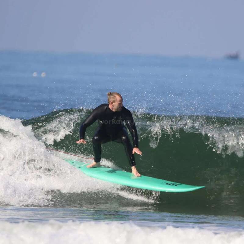 A surfer in a black wetsuit is skillfully riding a turquoise surfboard on a breaking wave in the ocean, enjoying the sunny, clear day.