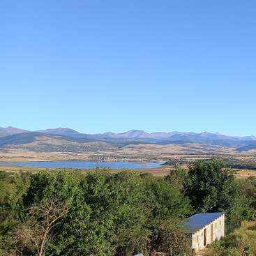 The image depicts a serene landscape featuring a small building, trees, a lake, and mountains under a clear blue sky, evoking a sense of tranquility and natural beauty.