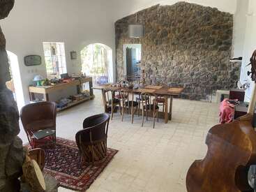 L'image représente une pièce spacieuse aux murs blancs et au sol carrelé, avec une table à manger, des chaises et un mur d'accent en pierre, la lumière naturelle pénétrant par les fenêtres.