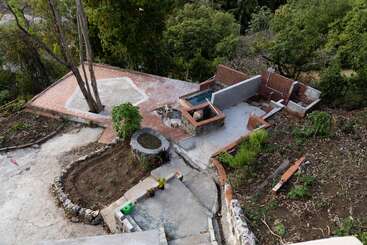 L'image représente une arrière-cour avec une piscine, entourée d'un patio, d'une clôture et d'un portail, avec un grand arbre à l'arrière-plan, dans un cadre extérieur naturel.