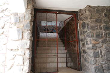 L'image montre un escalier avec une rampe à gauche et un mur à droite, avec une rampe et un mur, avec un escalier en arrière-plan. Les murs sont en pierre.