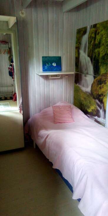 Une petite chambre confortable avec un lit simple, un oreiller rayé, une couverture rose, un tableau de chutes d'eau, un tableau de bateaux, une armoire à glace et des panneaux de bois.