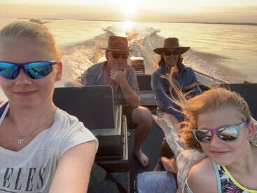 Un groupe de quatre personnes, portant toutes des lunettes de soleil, profitent d'une promenade en bateau sur un plan d'eau calme pendant le coucher du soleil, souriant et capturant ensemble ce moment pittoresque.