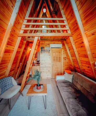 Essa cabana aconchegante com estrutura em A tem paredes de madeira quente, uma área de loft, móveis modernos, um sofá confortável, mesa pequena, planta interna e iluminação natural convidativa.