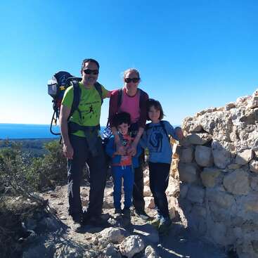 L'image représente une famille de quatre personnes posant pour une photo sur un affleurement rocheux, avec une vue panoramique de la mer et du ciel en arrière-plan.