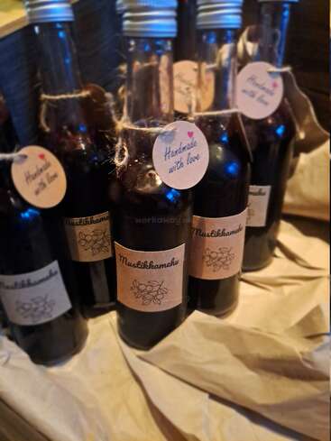 Five glass bottles of dark berry juice labeled "Mustikkamehu" and "Handmade with love", adorned with twine, are arranged on crumpled brown paper. Cozy handcrafted vibe.