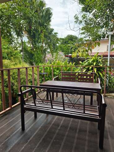 Bancos y una mesa de madera se encuentran en una terraza, rodeados de exuberantes plantas y árboles, creando un espacio exterior tranquilo y acogedor.
