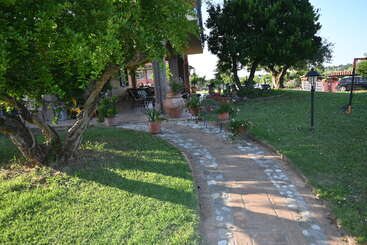 The image depicts a serene outdoor setting, featuring a house with a large yard, a patio area, and a well-manicured lawn, surrounded by trees and bushes. The scene exudes tranquility and natural beauty.
