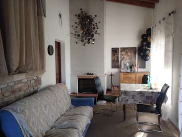 Un salon confortable avec un canapé à motifs, une horloge murale décorative, une cheminée, une table à manger avec quatre chaises, une œuvre d'art représentant un lion, des armoires et de grandes fenêtres avec des rideaux.
