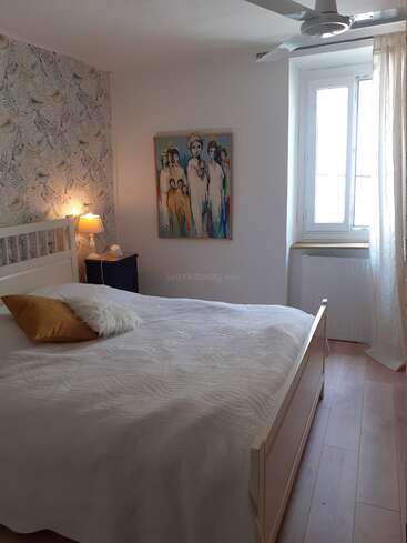 The image depicts a serene bedroom with a white bed, a vibrant painting on the wall, and a window adorned with a curtain, exuding a sense of calmness and tranquility.