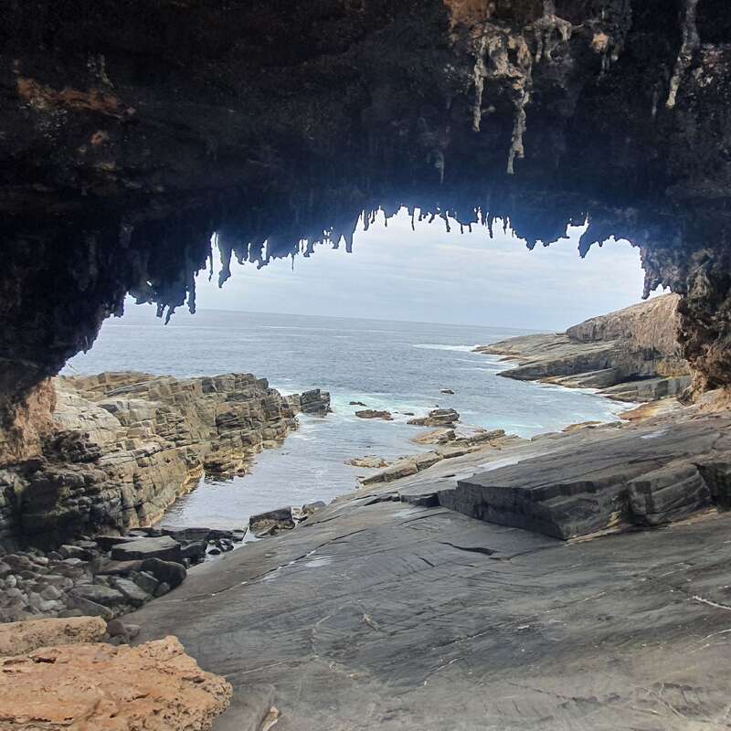 La imagen representa una cueva con vistas a un océano rocoso, con una costa escarpada y una vasta extensión de agua bajo un cielo nublado.