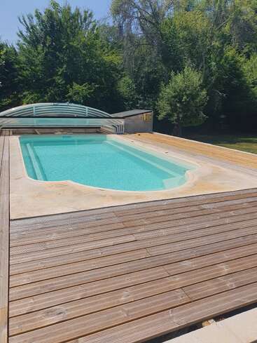 Uma piscina tranquila, cercada por um deck de madeira, fica bem no meio de um jardim cheio de vegetação, aproveitando o sol do verão, com árvores dando um clima relaxante.