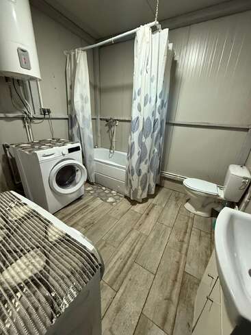 This room combines laundry and bathroom functions, featuring a washing machine, dryer, bathtub with shower curtain, toilet, sink, tiled floor, and water heater.