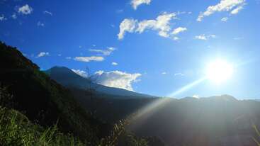 The image depicts a serene landscape with a mountain range, featuring a prominent tree in the foreground, set against a clear blue sky with a few clouds, evoking a sense of natural beauty.