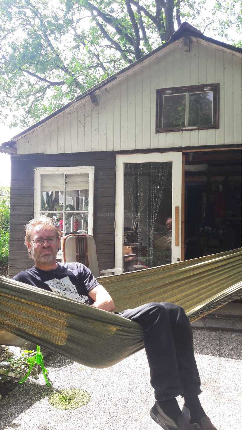 The image depicts a man sitting in a hammock outside a weathered house, with a suitcase visible through the window and a serene outdoor setting.