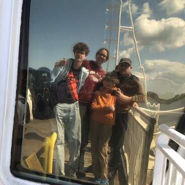 Four people are reflected in a window, standing closely together on a sunny day. There are clouds in the sky and railings in the background.