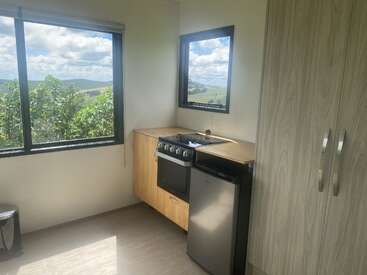 La cuisine compacte comprend une cuisinière, un mini-réfrigérateur, une grande armoire et des fenêtres offrant une vue panoramique sur les collines verdoyantes et le ciel bleu, créant ainsi une atmosphère lumineuse.