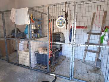 Dieses Bild zeigt ein sauberes Tierheim oder einen Zwinger mit Drahtgehegen, verschiedenen Vorräten, Hundeleinen, Kisten, einer Leiter und einigen hängenden Handtüchern und Taschen.