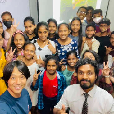 Un alegre grupo de niños y dos adultos posan juntos en el interior, sonriendo y haciendo el signo de la paz, creando un ambiente animado y acogedor en lo que parece una divertida reunión.