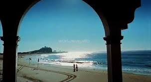The image depicts a serene beach scene through an archway, with a couple strolling along the shore and a large structure visible in the distance.