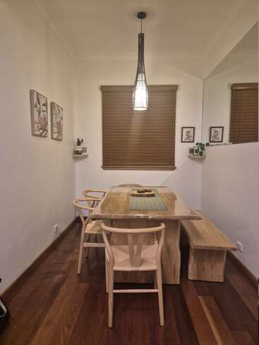A cozy dining area features a wooden table, matching chairs, and bench. Warm lighting, modern art, potted plants, and a large wall mirror create a welcoming ambiance.