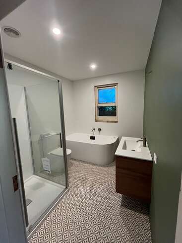 Este moderno cuarto de baño cuenta con suelo de baldosas estampadas, una ducha a ras de suelo, un mueble de baño suspendido, una bañera independiente, una pared decorativa en tonos verdes, una ventana pequeña, accesorios minimalistas e iluminación empotrada.