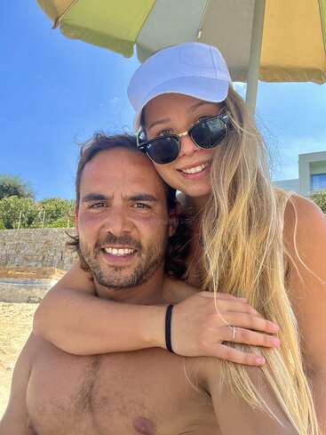 The image depicts a man and woman embracing on a beach, with the woman\'s arm wrapped around the man\'s neck and her hand resting on his shoulder.