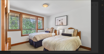 Este quarto aconchegante tem duas camas de solteiro, roupa de cama em tons neutros, janelas amplas com caixilhos de madeira, um abajur e uma gravura de um urso polar na parede.