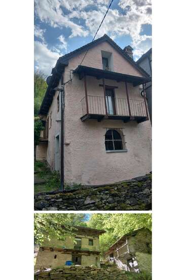 The image shows two rustic, stone-walled houses. The upper house is pink with a balcony, while the lower house appears weathered, surrounded by greenery and forest.
