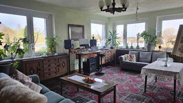 Dieses gemütliche Wohnzimmer besticht durch große Fenster, üppige Zimmerpflanzen, Vintage-Teppiche, bequeme Sofas, ein Mischpult, gemusterte Kissen und einen Tisch mit einem Obstarrangement als Tischdekoration.